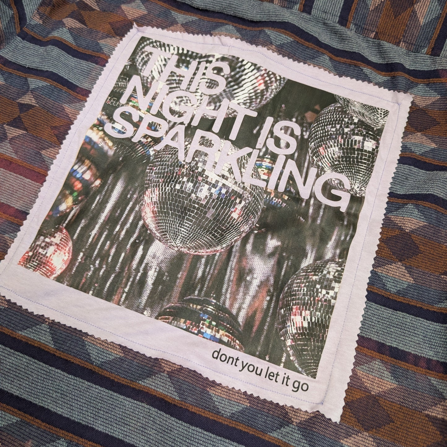 Textile with a patch that says 'This Night is Sparkling' on a patterned fabric background