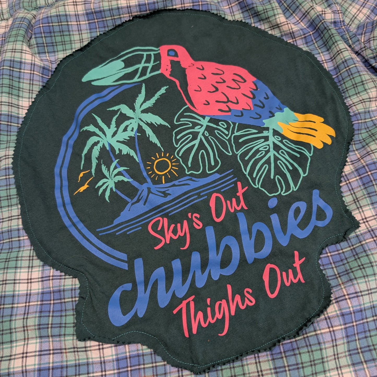 Embroidered patch with tropical design and text on a plaid fabric background