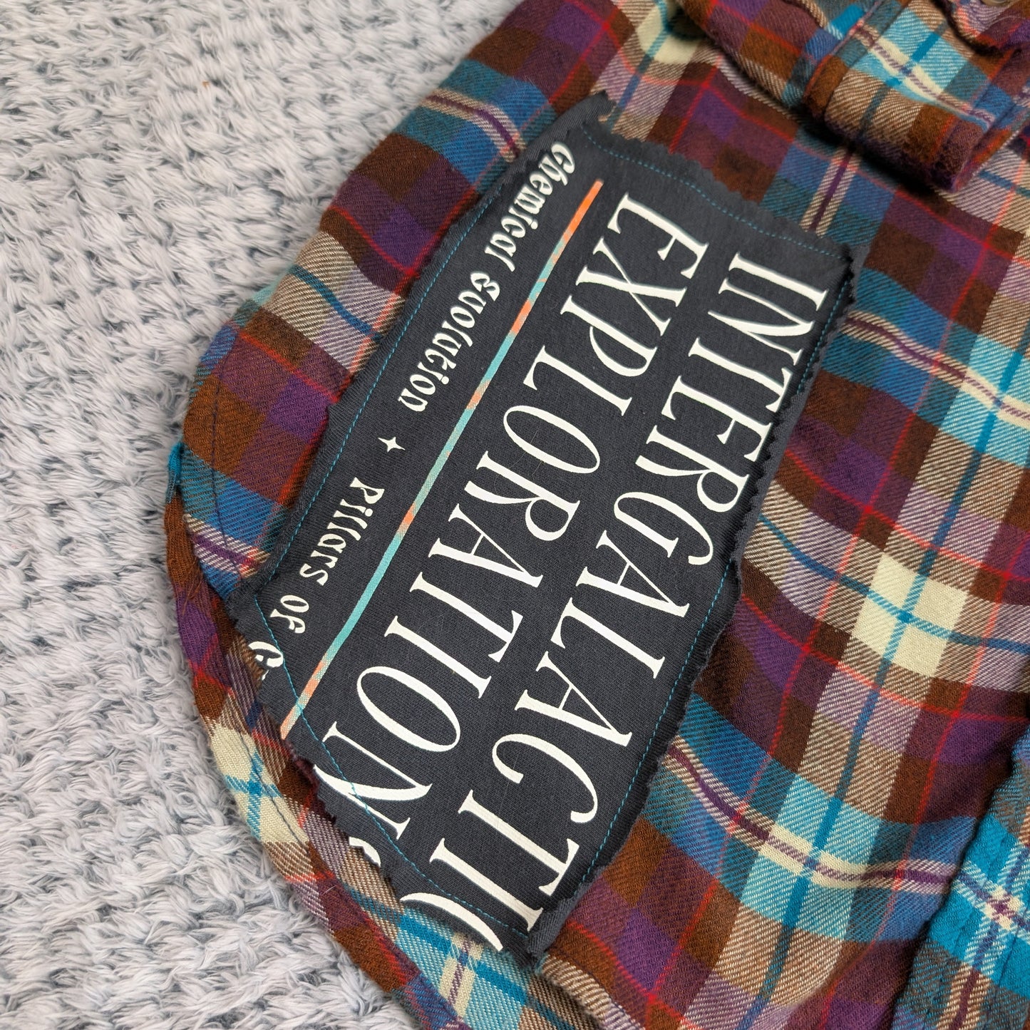 Plaid shirt with a patch labeled 'Exploration' on a textured surface