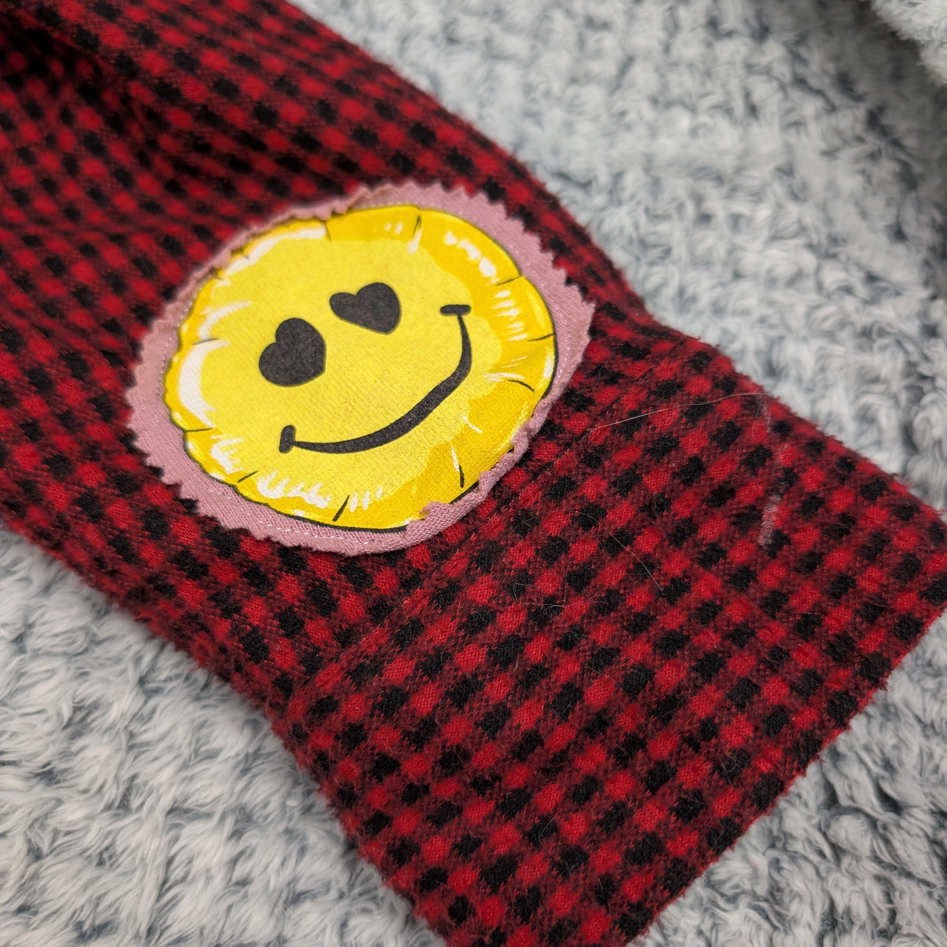 Red and black checkered fabric with a yellow smiley face patch on a gray surface