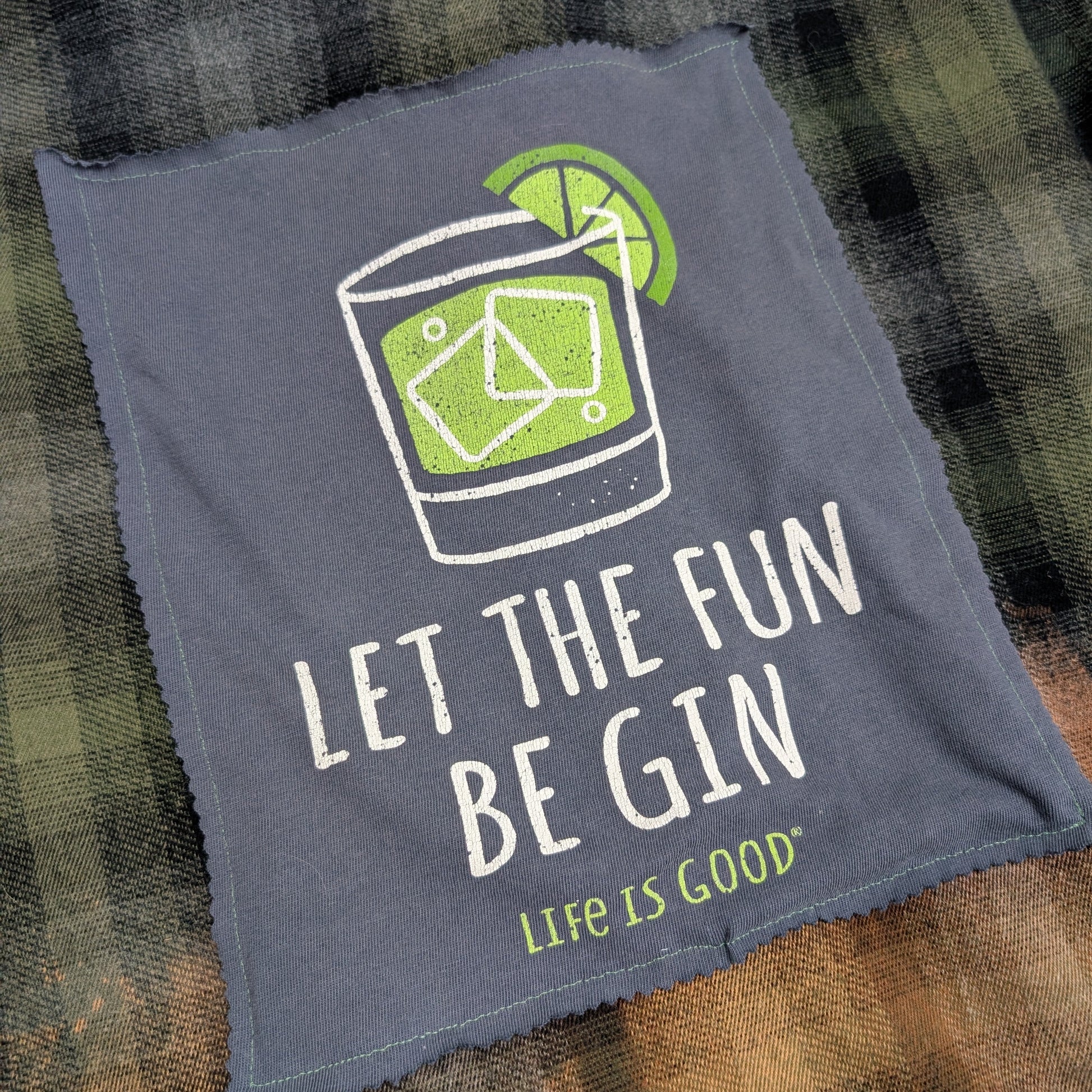 Gray towel with 'Let the Fun Be Gin' text and lime graphic on a plaid fabric background