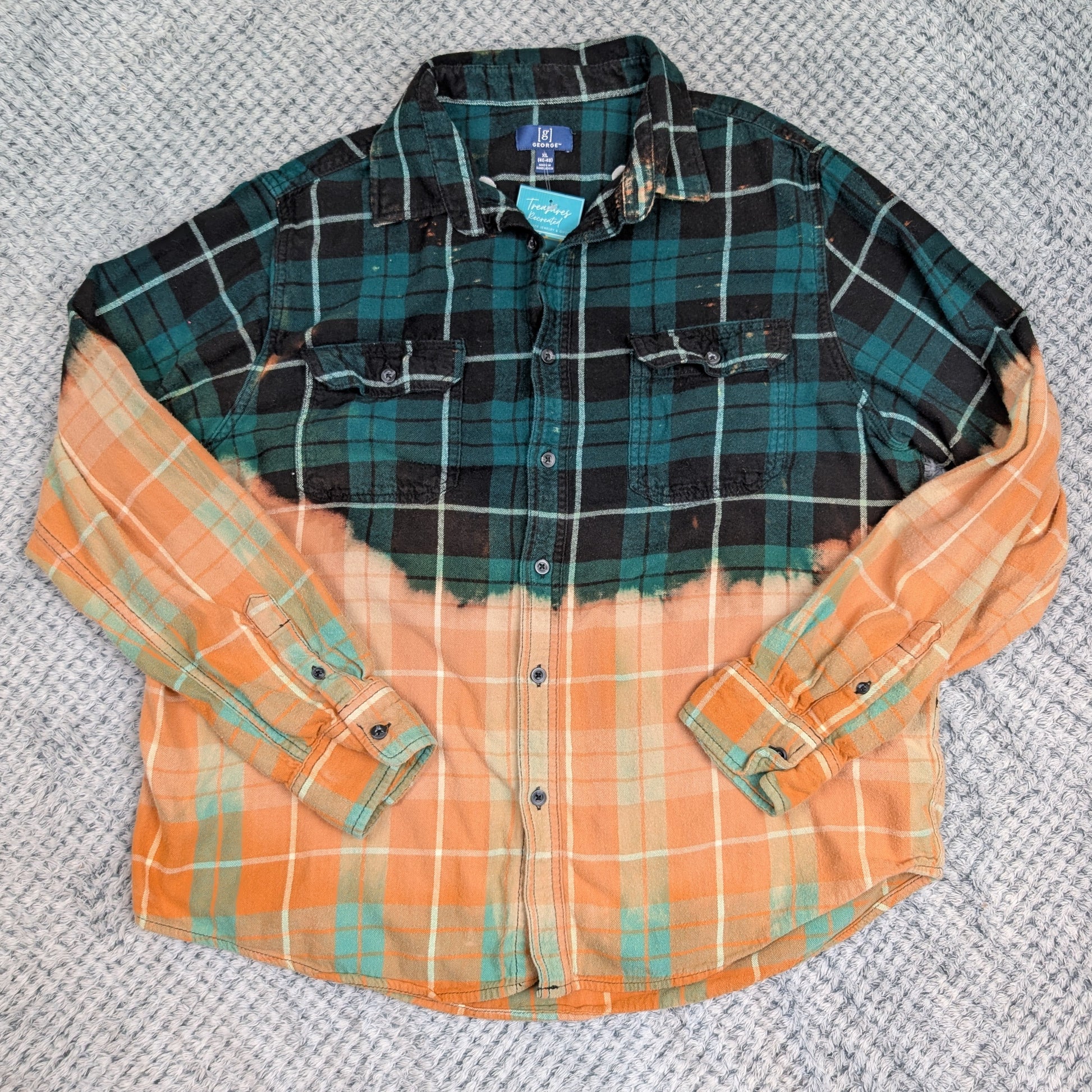 Plaid shirt with green and black top half and orange and green bottom half on a textured gray background