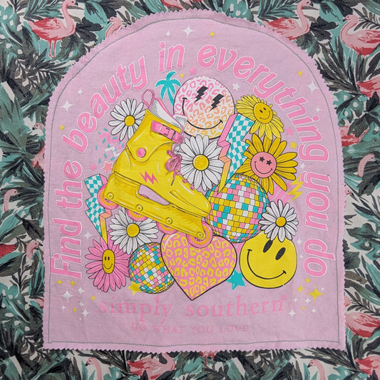 A pink arched fabric patch with a colorful cartoon illustration and the text 'Find the beauty in everything you do' laid flat on a green and pink tropical floral fabric.