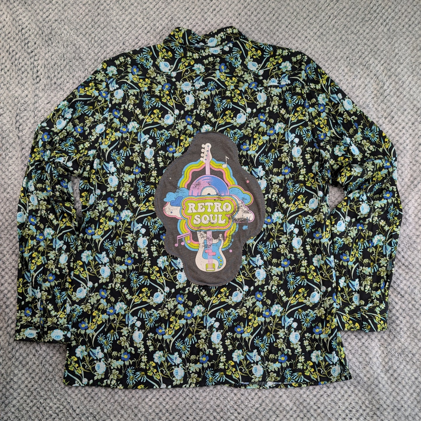 A long-sleeve button-up shirt with a black background and a dense multicolor floral print, featuring a large 'Retro Soul' patch on the chest.