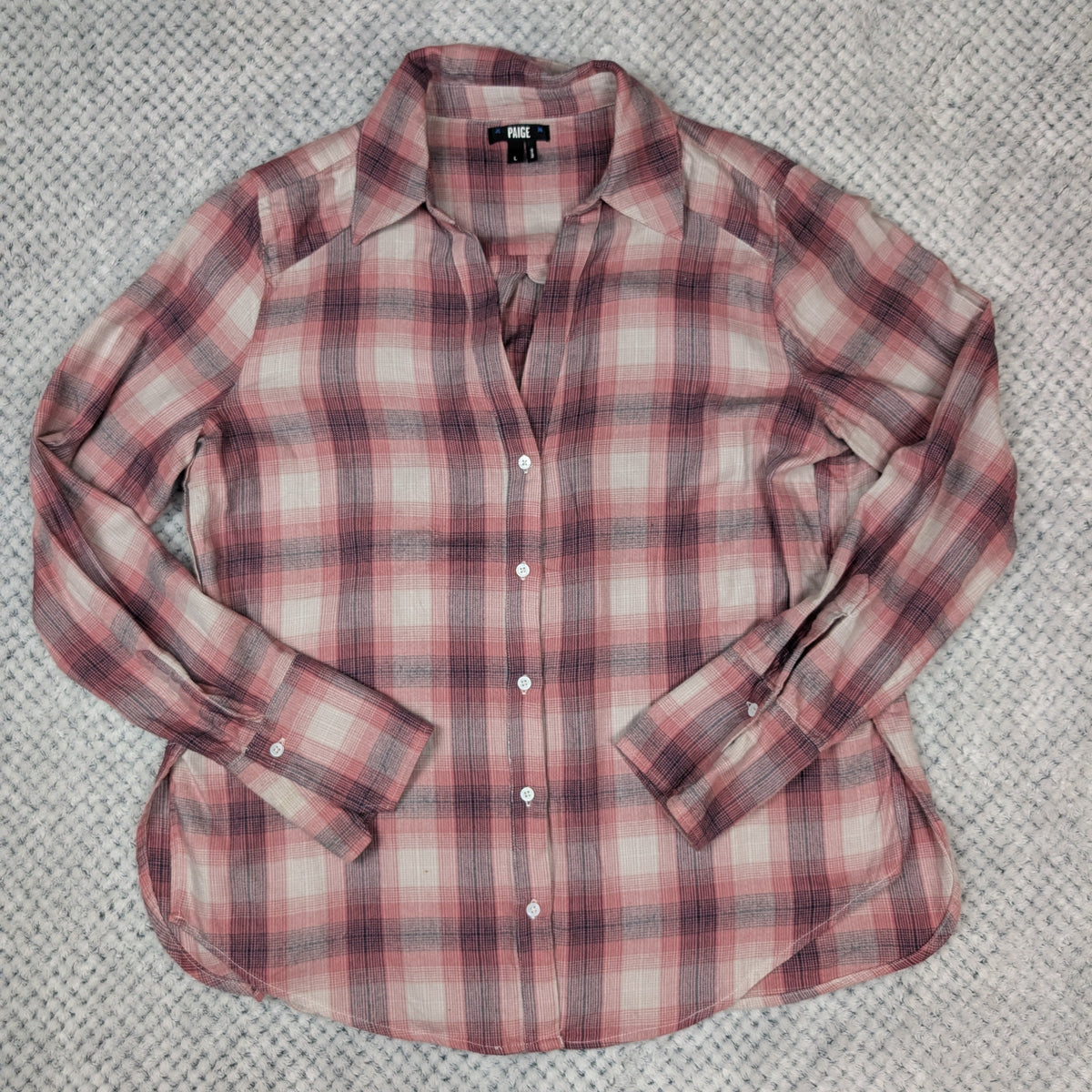 A long-sleeve plaid button-up shirt in pink, red, and white, laid flat on a textured gray fabric background.
